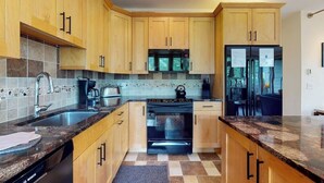 A kitchen with wooden cabinets, a Bosch dishwasher, a microwave, a stove, and a refrigerator. - Bright Mountain Retreat w/Shared Pool & Hot Tub & Mountain Views from Balcony (Vail)