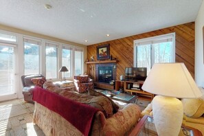 A living room with a fireplace, a television, and a lamp. - Western-inspired condo w/ wood fireplace, full kitchen, & shared hot tub & pool (Vail)