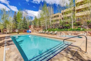 A swimming pool with a stone wall, lounge chairs, and a building with a wooden facade. - Western-inspired condo w/ wood fireplace, full kitchen, & shared hot tub & pool (Vail)