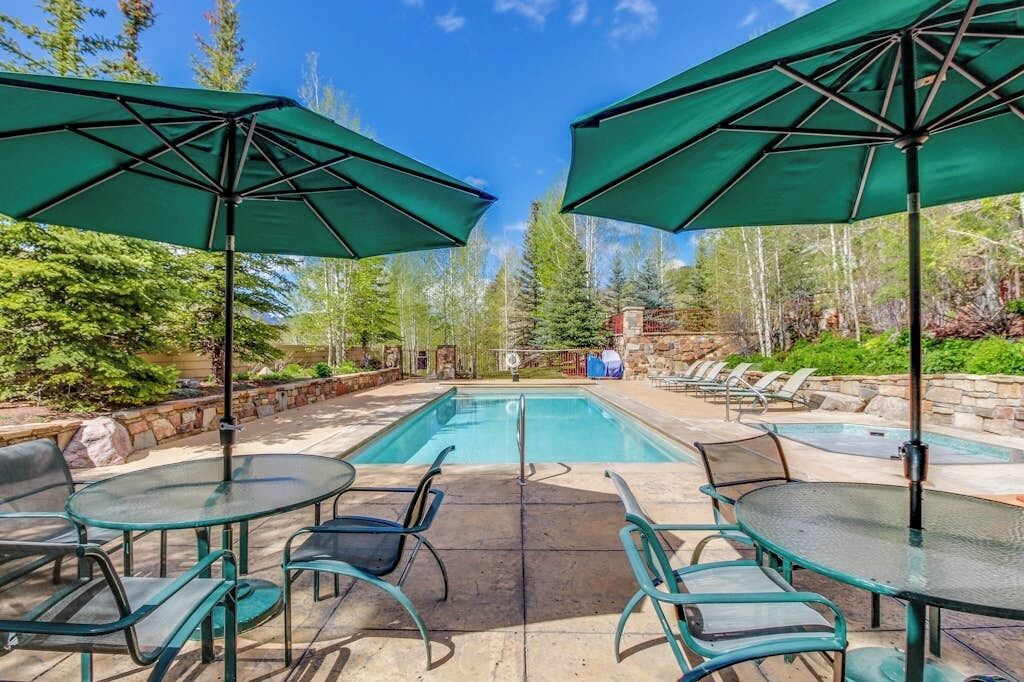 A pool area with two umbrellas, glass tables, and chairs.
