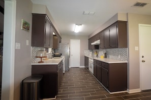 A kitchen with dark cabinets, a white countertop, a stainless steel refrigerator, and a tiled backsplash.