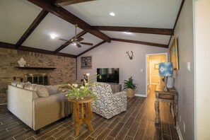 A living room with a sofa, a patterned chair, a television, and a fireplace. - Peaceful Small-Town Retreat with Everything Just Minutes Away (Longview)