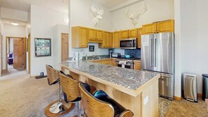 Una cucina moderna con mobili in legno, piani in granito, un frigorifero in acciaio inossidabile e un forno a microonde.