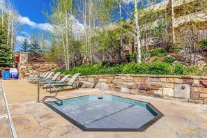 A swimming pool with a stone border, lounge chairs, and a stone wall with greenery. - Mtn-view condo next to lifts with heated outdoor pool, hot tub, sauna, fireplace (Vail)