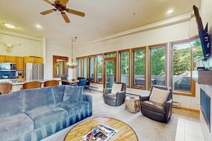 A spacious living area with a large sofa, a coffee table, and a fireplace. There is a dining area with a table and chairs, and a kitchen with modern appliances. - Mtn-view condo next to lifts with heated outdoor pool, hot tub, sauna, fireplace (Vail)