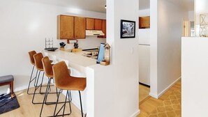 Een moderne keuken met houten kastjes, een wit aanrecht en barstoelen.