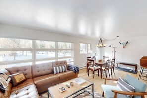 A living room with a brown leather sofa, a coffee table, and a dining area with wooden chairs and a table. - Charming and stylish condo with pool, hot tub, washer/dryer, & WiFi (Vail)