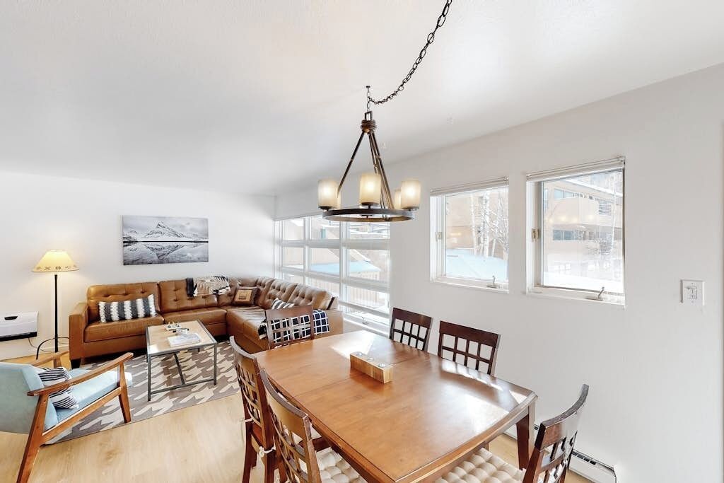 A modern living room with a wooden dining table, a sofa, and a chandelier.