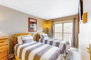 Ein Schlafzimmer mit zwei Betten, einer Holzkommode, einem Poster, einer Lampe und einem Fenster mit Vorhängen.