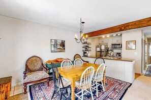 Ein Essbereich mit Holztisch und Stühlen, einem gemusterten Teppich und einer Küche im Hintergrund.