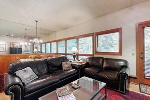 Ein Wohnzimmer mit Ledersofas, einem Glastisch und einem Essbereich mit Holzsesseln und einem Tisch.