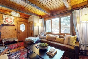Ein gemütliches Blockhaus-Interieur mit einer Couch, einem Couchtisch mit Pflanze, einem Schild der Skiregierung und einem großen Fenster.