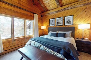 Ein Schlafzimmer einer Holzhütte mit einem Bett, Nachttischlampen und gerahmten Bildern an der Wand.