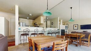 Un coin repas avec une table et des chaises en bois, une cuisine à l’arrière-plan et un salon avec un canapé.