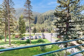 A view of a parking lot with several cars, surrounded by trees and a mountain in the background. - Cozy condo with fireplace, pool & hot tub - steps to ski shuttle (Vail)