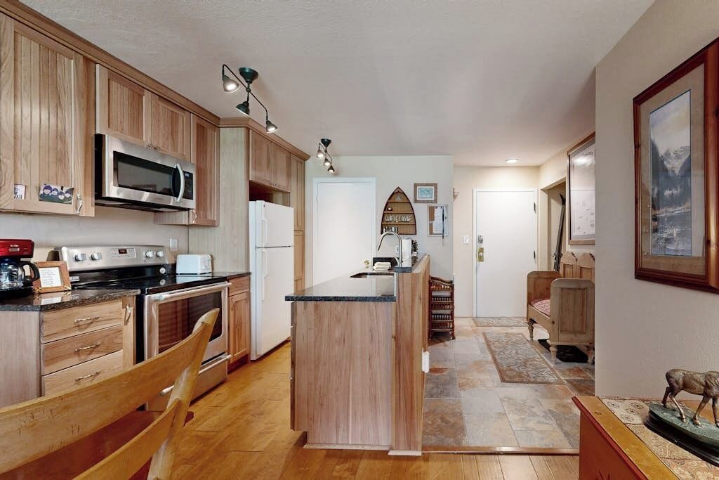Cucina con mobili in legno, forno a microonde, fornello e zona pranzo con una sedia.