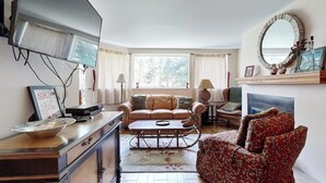 A living room with a sofa, a coffee table, a TV, and a fireplace. - Adorable Condo in w/Shared Pool, Hot Tub, WiFi, Washer/Dryer, & Free Shuttle (Vail)