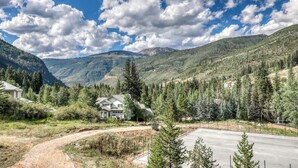 A residential area with houses, a paved driveway, and a mountainous backdrop. - Beautiful East Vail Condo w/ Vail Village Ski Lockers/Free WiFi/Near Ski Shuttle (Vail)