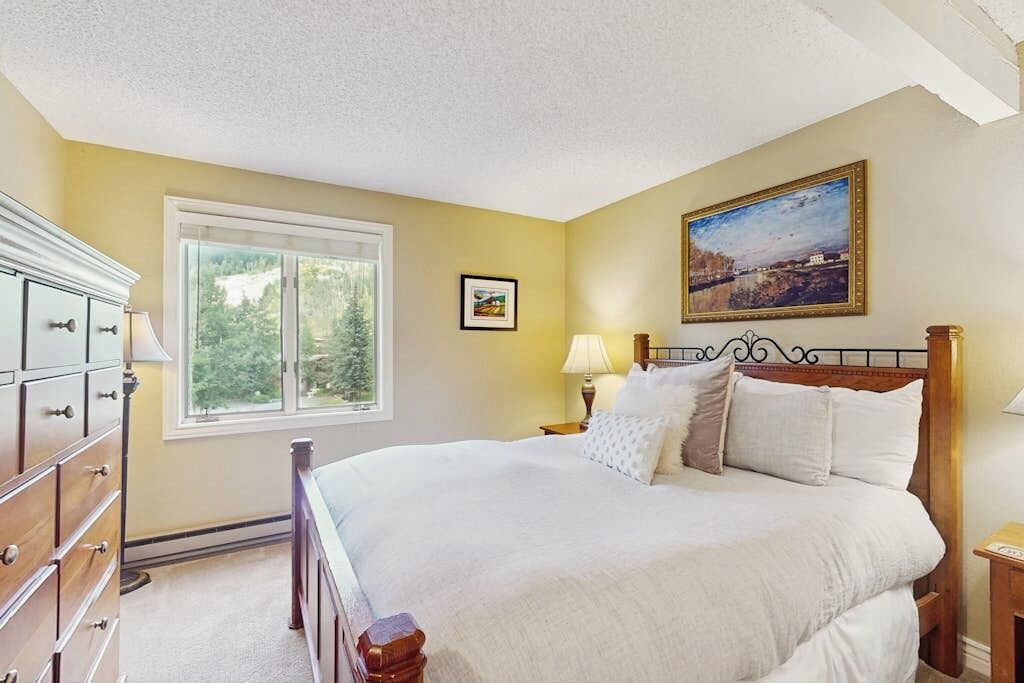 A bedroom with a bed, dresser, window, and wall art.