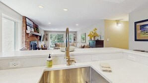 A modern kitchen with a central island, stainless steel sink, and a brick accent wall. - Beautiful East Vail Condo w/ Vail Village Ski Lockers/Free WiFi/Near Ski Shuttle (Vail)