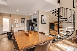 Ein Essbereich mit Holztisch und Stühlen, eine Küche mit modernen Geräten und eine Wendeltreppe.