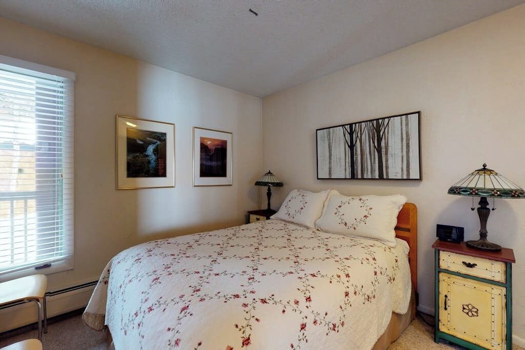 A bedroom with a bed, a nightstand, a lamp, and two framed pictures on the wall.