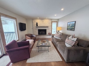 A living room with a fireplace, a television mounted on the wall, a sofa, a chair, and a coffee table. - Cozy East Vail condo - Mountain view, Hot Tub, Pool & W/D - Near Ski shuttle (Vail)