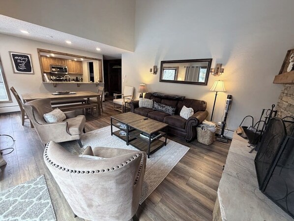 Ein modernes Wohnzimmer mit einer Couch, Sesseln, einem Couchtisch, einem Kamin und einer Küchenzeile.