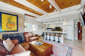 A spacious living room with a fireplace, leather sofa, and a kitchen area with white cabinets and bar stools. - Ski-in/out hotel-condo with amazing mountain views, pool, hot tub, & balconies (Vail)
