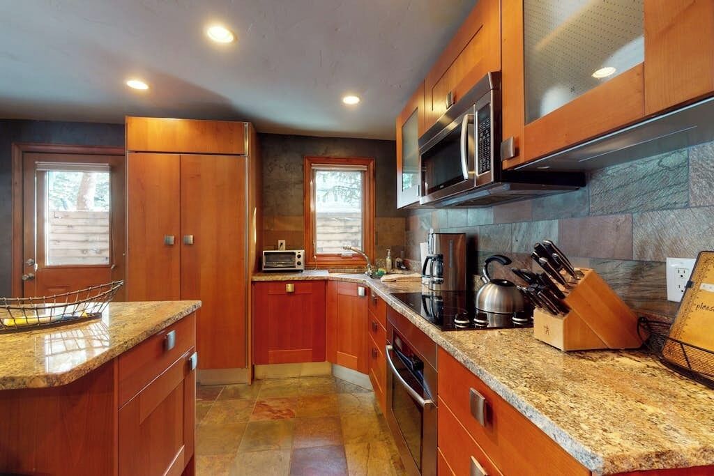 A kitchen with wooden cabinets, granite countertops, a microwave, a toaster, and a knife block.