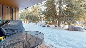 Uma área de estar coberta ao ar livre, com churrasqueira, mesa e vista para árvores cobertas de neve.