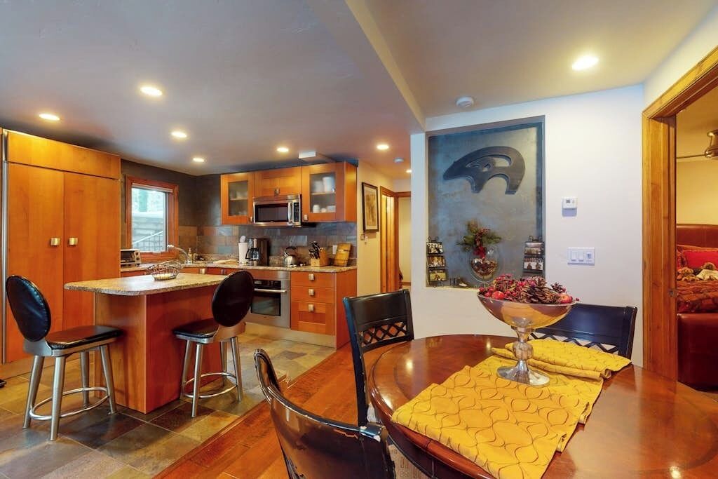 A modern kitchen with wooden cabinets, a central island, and a dining area with a table and chairs.