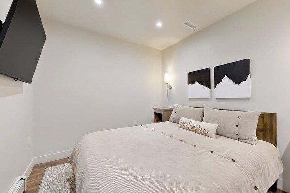 Une chambre à coucher comprenant un lit, un téléviseur à écran plat fixé au mur et deux œuvres d’art accrochées au mur.
