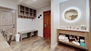 Ein Badezimmer mit Holzwaschtisch, einem runden Spiegel mit Beleuchtung, einer Bank und einer Tür mit Ablage darüber.