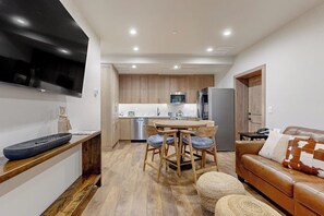 Eine moderne Küche mit Holzschränken, einem Essbereich mit rundem Tisch und Stühlen, einem Ledersofa und einem flachbildfernseher an der Wand.