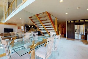 Ein modernes Interieur mit einem Glastisch, weißen Stühlen, einer Holztreppe und einer Küchenzeile.