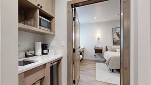 Une petite pièce comprenant un coin cuisine, un lit, une table de chevet et un tableau accroché au mur.