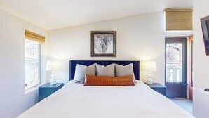 Una habitación de hotel con una cama grande, dos mesitas de noche con lámparas, una obra de arte enmarcada sobre la cama y una ventana con persianas.