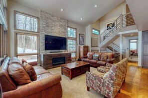 A spacious living room with a fireplace, leather sofas, a patterned armchair, and a staircase leading to an upper level. - Townhome w/ Gorgeous View, Gas Fireplace & Fast WiFi - Steps to Ski Shuttle (Vail)