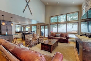 A spacious living area with leather sofas, a coffee table, and a TV. Large windows offer a view of a snowy landscape. - Townhome w/ Gorgeous View, Gas Fireplace & Fast WiFi - Steps to Ski Shuttle (Vail)