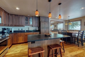 A kitchen with wooden cabinets, a central island, bar stools, pendant lighting, and a dining area with chairs and a table. - Townhome w/ Gorgeous View, Gas Fireplace & Fast WiFi - Steps to Ski Shuttle (Vail)