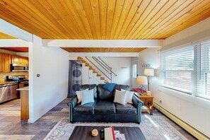 Ein modernes Wohnzimmer mit Ledersofa, Holzboden und einer Küche im Hintergrund, sowie einer Treppe, die nach oben führt.