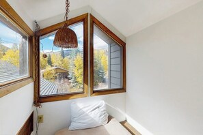 Ein Zimmer mit großem Fenster, einer Pendelleuchte und einem weißen Kissen auf dem Bett.
