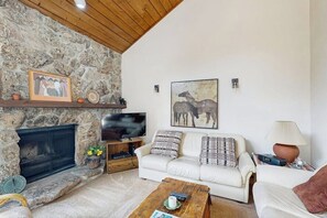 Ein Wohnzimmer mit Kamin aus Stein, einem weißen Sofa, einem Couchtisch und einem Fernseher.