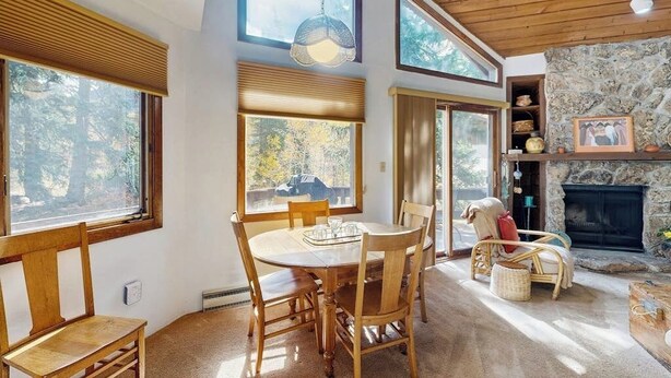 A cozy room with a stone fireplace, wooden furniture, and large windows offering a view of the outdoors. - Quiet, multi-level townhome with great location & mountain views (Vail)