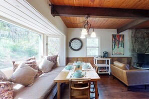 A cozy living room with a wooden ceiling, a dining table set for four, a sofa with cushions, and a fireplace. - Quiet mountain-view condo with patio, fireplace & grill - walk to Vail bus (Vail)
