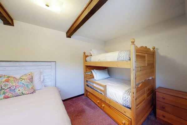 A bunk bed with a wooden headboard, a single bed with a patterned pillow, and a wooden dresser. - Quiet condo with private patio, grill and wood-burning fireplace (Vail)