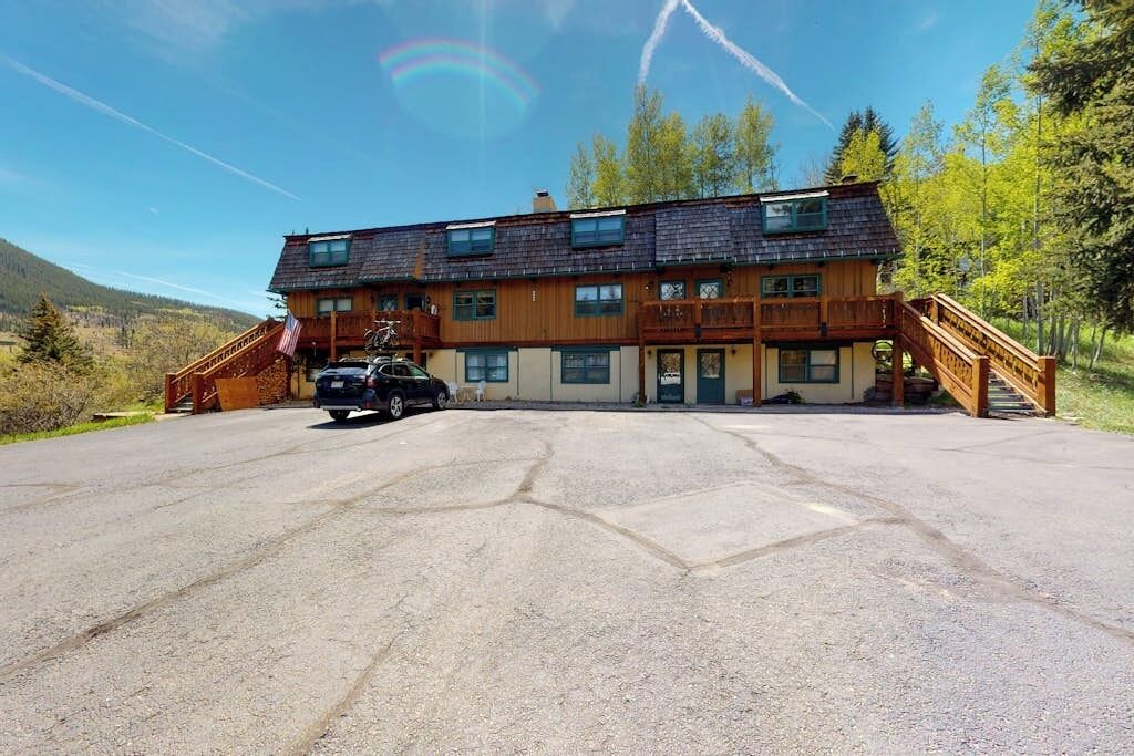 A two-story wooden building with a covered driveway, a staircase, and a vehicle parked in front.