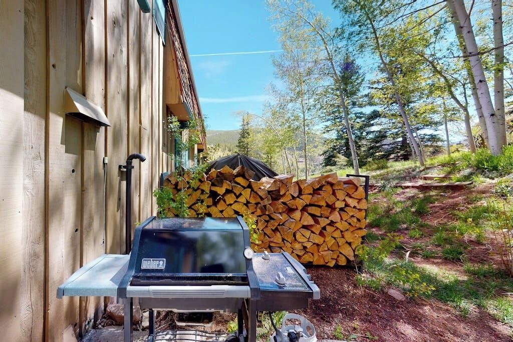 Una parrilla Weber al aire libre, con una pila de leña cerca.