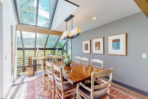 A dining area with a wooden table, chairs, a vase, and framed pictures on the wall. - Mountain-view home with private hot tub, solarium & fireplace - steps to shuttle (Vail)